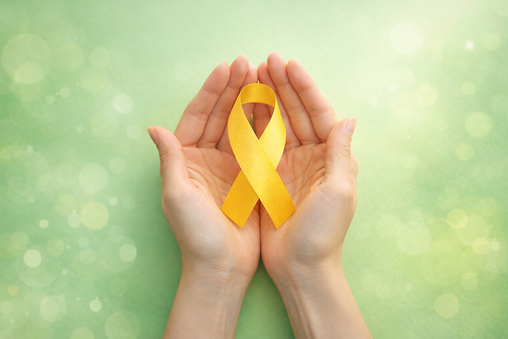 Manos sosteniendo un lazo amarillo sobre fondo verde suave, símbolo de esperanza y prevención del suicidio.